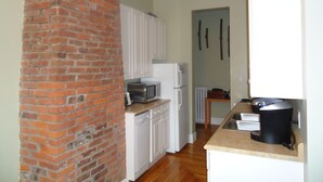 A kitchen with white cabinets, a brick wall, a microwave, a refrigerator, and a coffee maker. - Down Town Heritage Suite on Water Street           (Charlottetown)