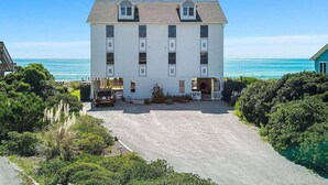 A two-story white building with a central entrance and a driveway leading to a parked car. - Panoramic Oceanfront home on Emerald Island. Close to everything!! (Emerald Isle)