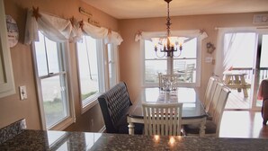 A kitchen with granite countertops, a dining table with chairs, a chandelier, and large windows with curtains. - Panoramic Oceanfront home on Emerald Island. Close to everything!! (Emerald Isle)