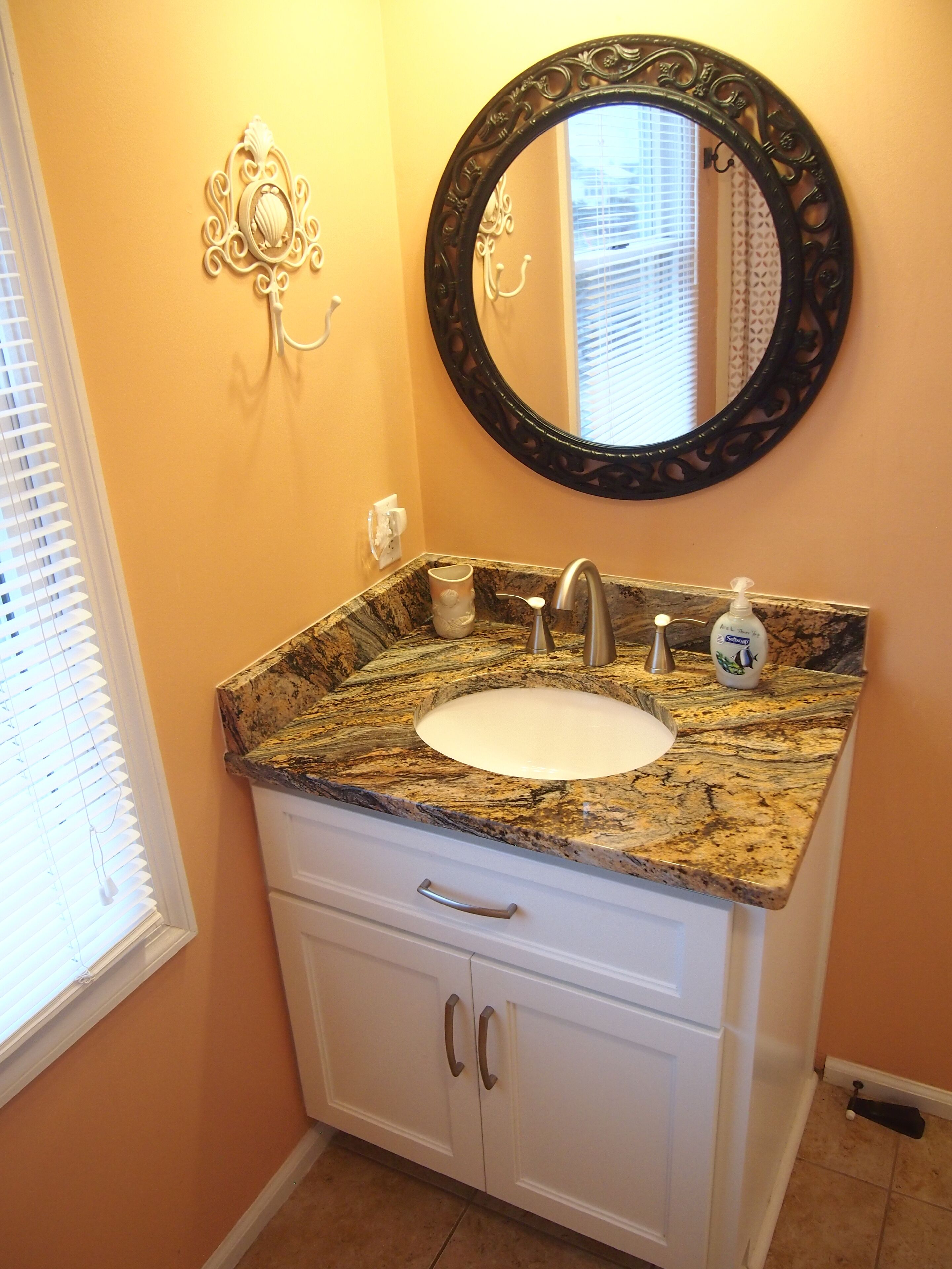 A bathroom with a granite countertop sink, a black ornate mirror, and a white cabinet with two doors.