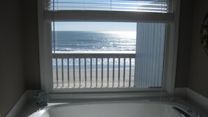 A bathroom with a large bathtub, a view of the ocean through a window, and a shower area. - Panoramic Oceanfront home on Emerald Island. Close to everything!! (Emerald Isle)