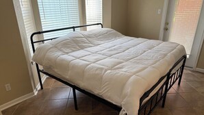 Un lit recouvert d’une couette blanche, dans une pièce aux murs de couleur beige et au sol carrelé.