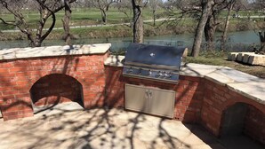An outdoor brick barbecue grill with a chimney, a built-in cabinet, and a view of a park with a lake. - River Front property (Seguin)