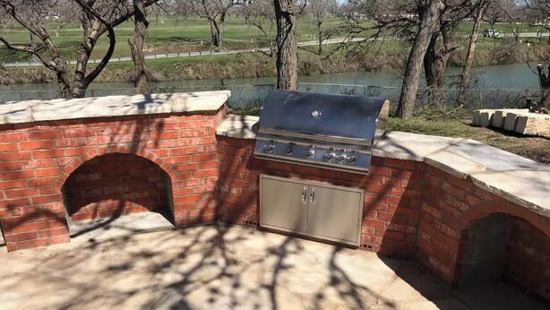 Un barbecue extérieur en briques, doté d’une cheminée, d’un meuble intégré et offrant une vue sur un parc avec un lac.