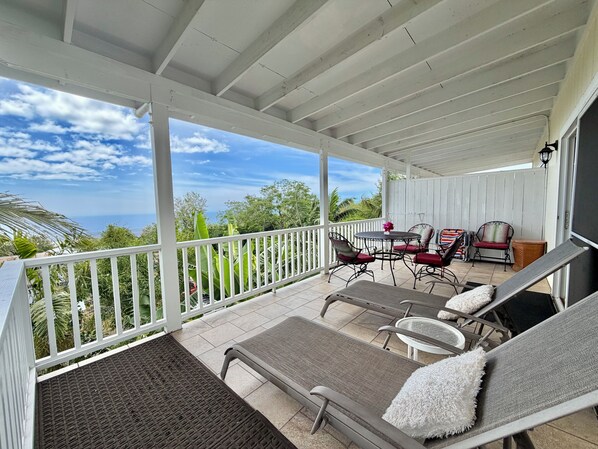 A covered outdoor area with a view of the ocean, a table with chairs, and a bench with a cushion.