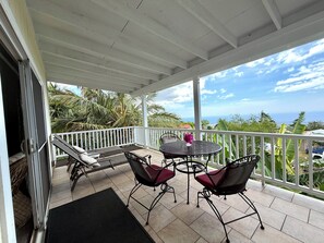 A covered outdoor seating area with a table and chairs, a view of the ocean, and a white railing.