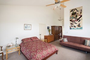Ein Schlafzimmer mit einem Bett, einem Schlafsofa, einem Holzkasten, einem Deckenventilator und einem Wandbild.