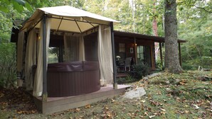 A cabin with a covered hot tub, a deck, and a view of the surrounding forest. - Cozy mountain cabin with amazing views, year round hot tub and pet friendly (Waynesville)