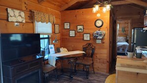 A cozy cabin interior with a wooden interior, a dining table with chairs, a television, and a refrigerator. - Cozy mountain cabin with amazing views, year round hot tub and pet friendly (Waynesville)