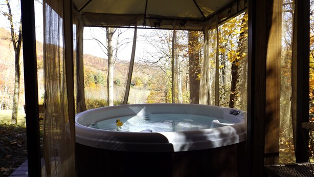 A hot tub in a covered outdoor area with a view of a forested landscape. - Cozy mountain cabin with amazing views, year round hot tub and pet friendly (Waynesville)