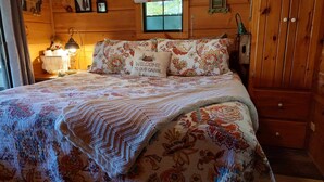 A cozy cabin bedroom with a floral-patterned bedspread, a welcome pillow, and a rustic wooden cabin sign. - Cozy mountain cabin with amazing views, year round hot tub and pet friendly (Waynesville)