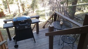 En träaltan med en grill, ett runt bord och stolar.