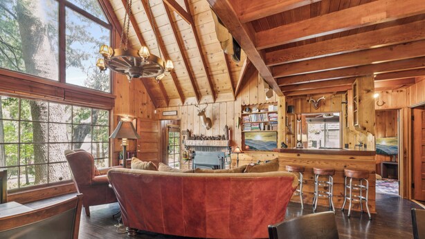 A log cabin interior with a fireplace, wooden furniture, and a view of the outdoors.