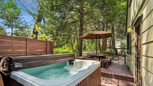 A hot tub on a wooden deck with a wooden fence, a table, and an umbrella.