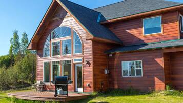 A two-story wooden house with a large deck and a gas grill.
