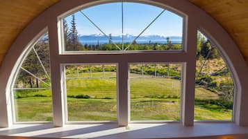 A room with a large arched window overlooking a grassy landscape and distant mountains.