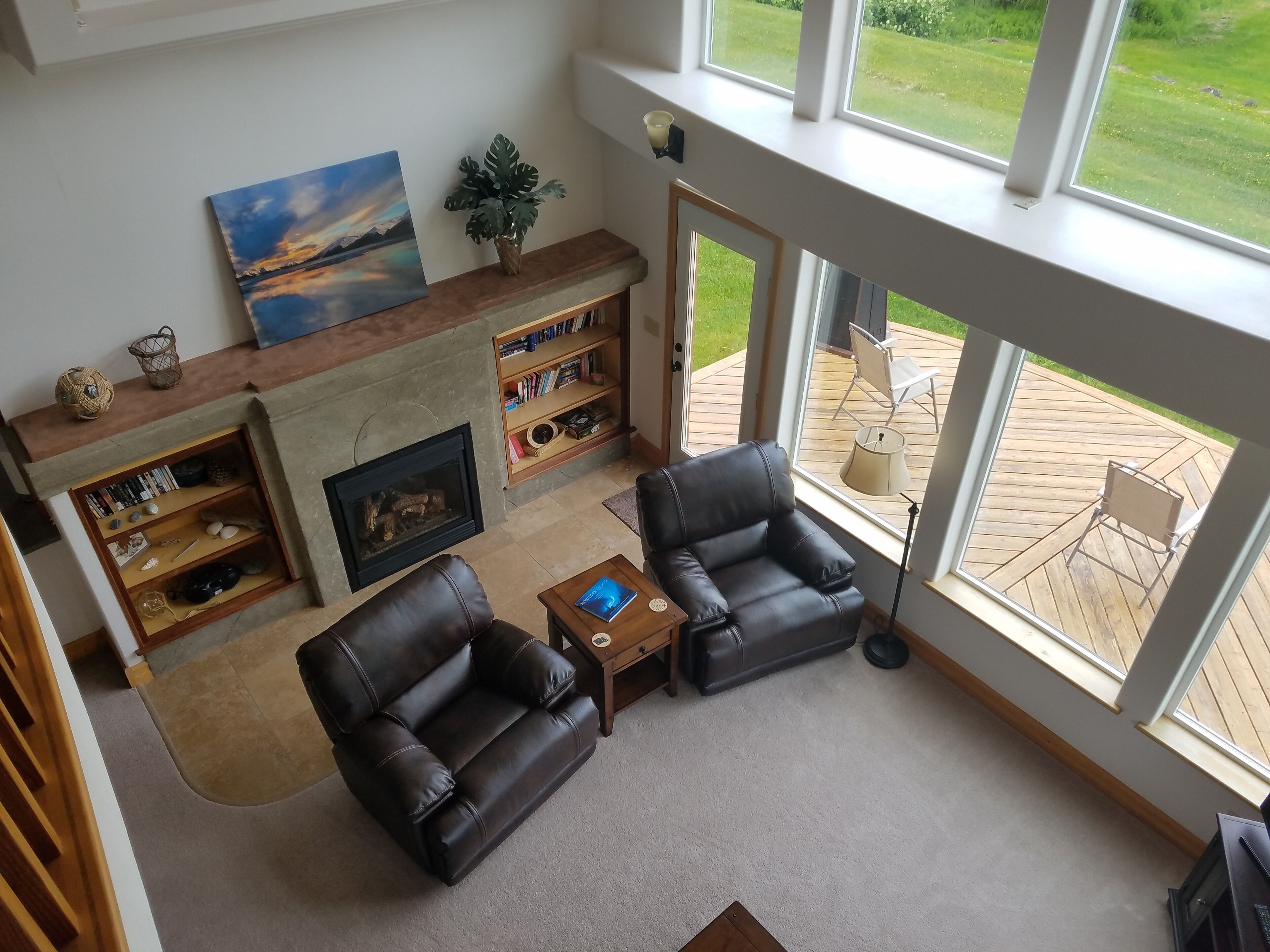 A living room with a fireplace, leather chairs, a bookshelf, and a view of the outdoors.