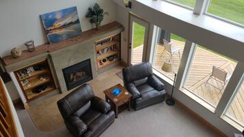 A living room with a fireplace, leather chairs, a bookshelf, and a view of the outdoors.