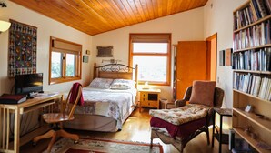 Un dormitorio acogedor con techo de madera, una cama, un escritorio con ordenador, una silla, una estantería y una ventana que deja entrar luz natural.