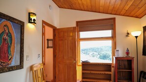 Puerta de madera que da a un cuarto con vista a un área boscosa. Una silla de madera y una pequeña mesa se ven en primer plano.