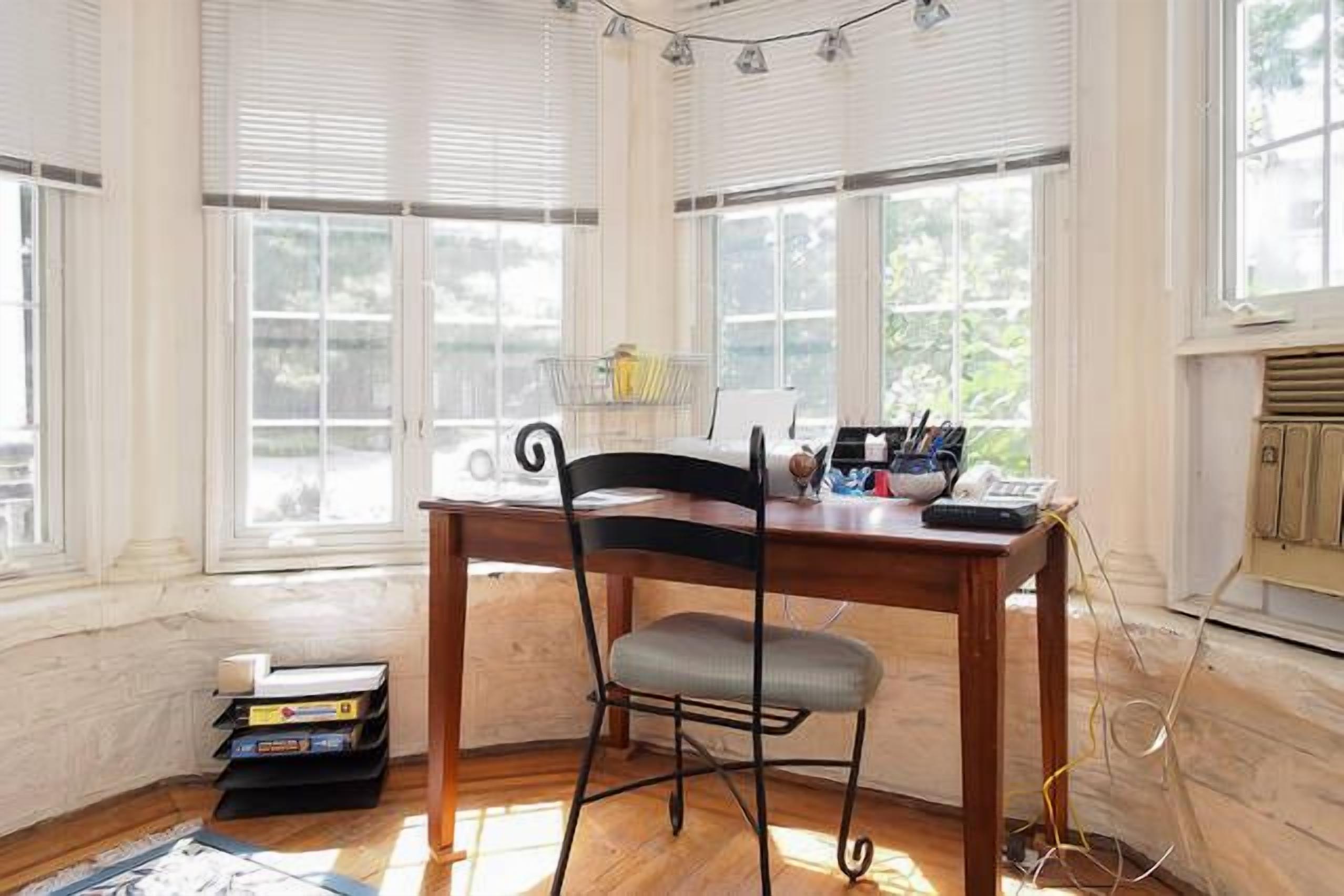 A room with a wooden desk, a chair, and a window with blinds.