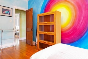 A bedroom with a wooden cabinet, a bed, and a colorful wall mural.