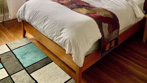 A bedroom with a wooden bed, a colorful quilt, a window with curtains, a ceiling fan, and a view of the outside. - Artsy Homey Rowhouse, 3bdrm & office, quiet urban area, free parking, fast WiFi (Baltimore)