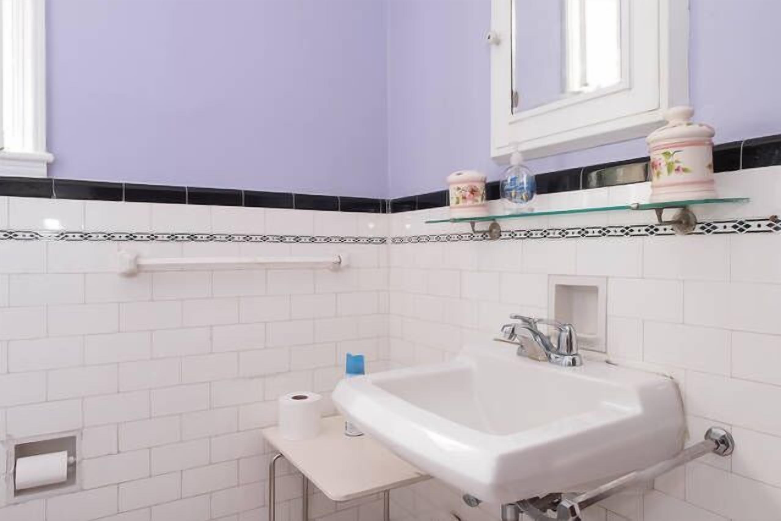 A bathroom with a white sink, a mirror above it, and a toilet paper holder on the wall.