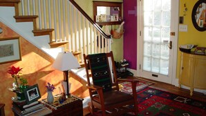 A staircase with wooden railings, a chair, a small table with a lamp, a rug, and a door with a window. - Artsy Homey Rowhouse, 3bdrm & office, quiet urban area, free parking, fast WiFi (Baltimore)