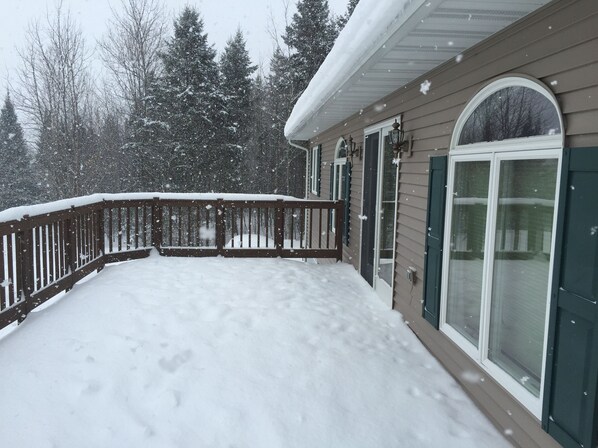 Une terrasse enneigée, dotée d’une rambarde en bois et d’une porte vitrée.
