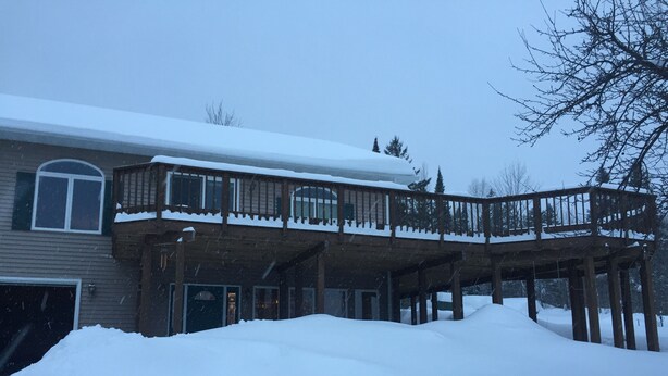 Una casa de dos pisos con un porche de madera y un techo cubierto de nieve.