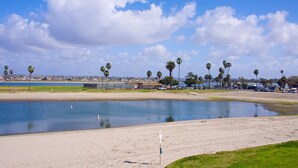 A sandy beach with a calm water body, palm trees, and a distant cityscape. - On the Beach!!  Perfect for Families.  Right on the Water (San Diego)