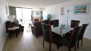 A living room with a glass dining table, dark chairs, a sofa, and a coffee table. There is a fireplace, a TV, and a painting on the wall. - On the Beach!!  Perfect for Families.  Right on the Water (San Diego)