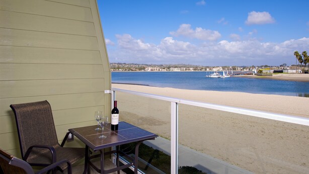 A balcony with a table, a chair, and a bottle of wine. The view includes a beach and a body of water with boats. - On the Beach!!  Perfect for Families.  Right on the Water (San Diego)
