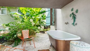 Une salle de bain avec une baignoire d’époque, un fauteuil en osier et un mur décoratif.