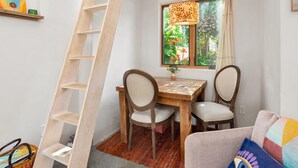 Une pièce chaleureuse avec une table et des chaises en bois, une échelle, une fenêtre donnant sur un paysage verdoyant et un coussin coloré sur un canapé.