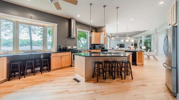 Una cucina moderna con pavimento in legno, un'isola centrale con sgabelli e un frigorifero capiente.