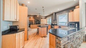 A modern kitchen with wooden cabinets, a stone accent wall, and a large island with a sink. - Family Vacations, Reunions, Anniversaries, Holidays, Graduations, Lakefront (Mooresville)