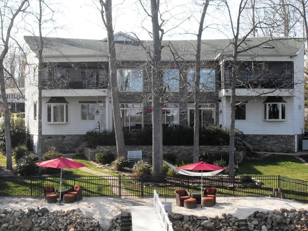 A two-story building with a stone foundation and white siding. There are outdoor seating areas with red umbrellas and stone walls.