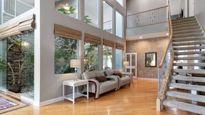 Un'ampia zona giorno con soffitto alto, una scala e grandi finestre.