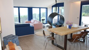 A modern living room with a wooden dining table, blue and pink sofas, and a large window with a view of greenery. - Modern Seaview Villa With Infinity-Pool (Palamos)