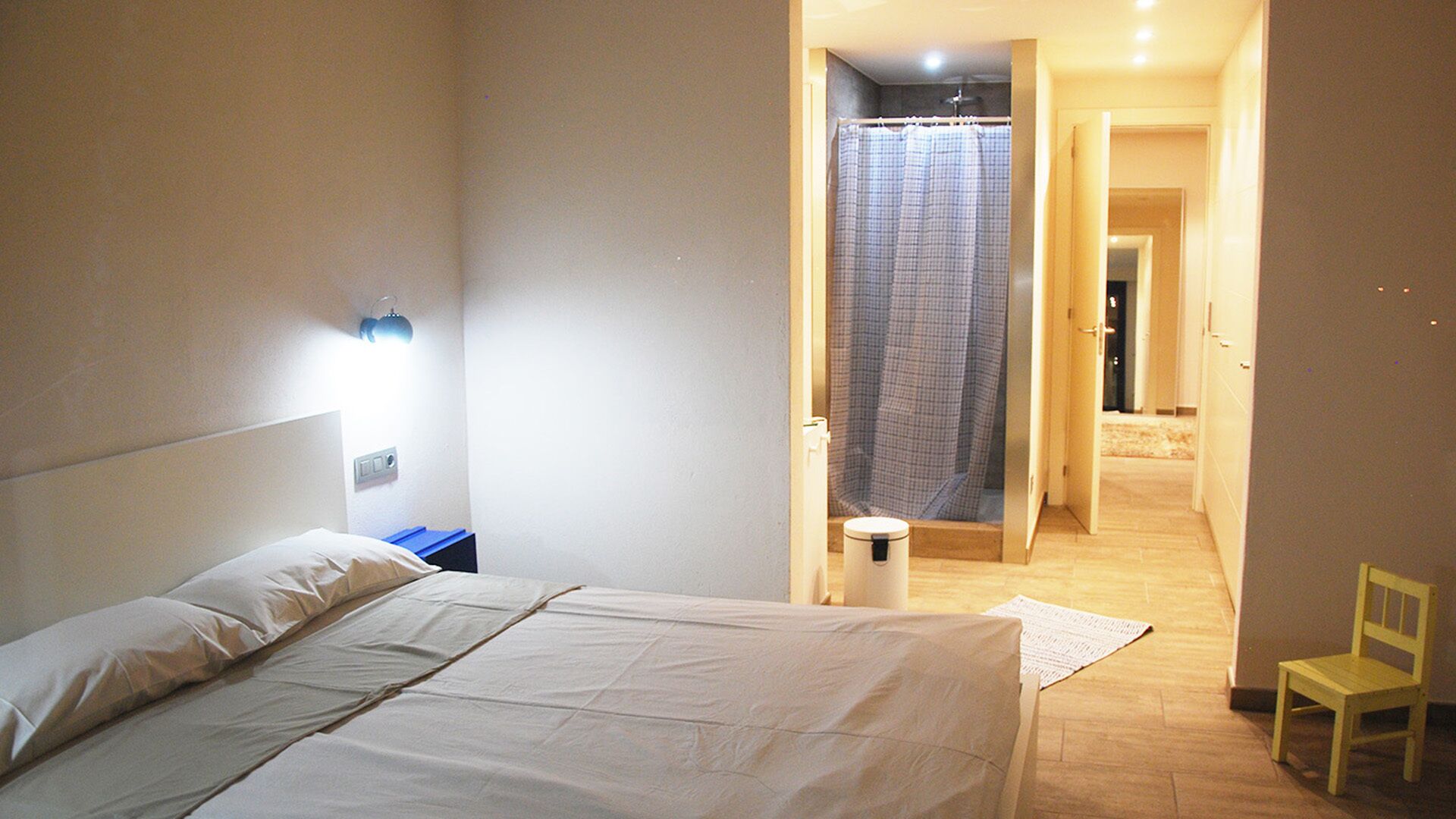 A hotel room with a bed, a nightstand, a chair, and a bathroom visible through an open door.