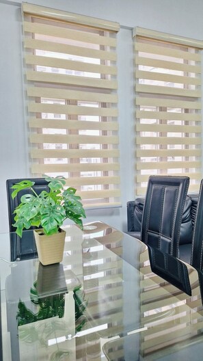 Une salle de conférence avec une table en verre, deux fauteuils en cuir, une plante en pot et des stores aux fenêtres.