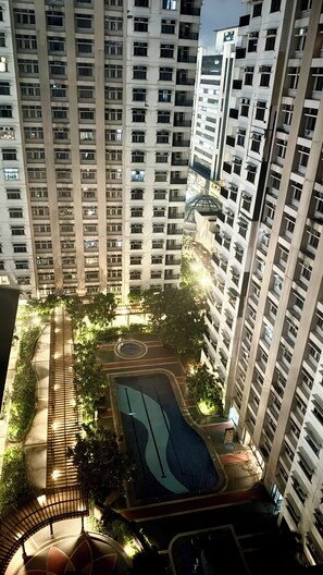 Un immeuble résidentiel de grande hauteur doté de nombreux balcons, d’une cour intérieure avec une piscine et d’un espace verdoyant environnant.
