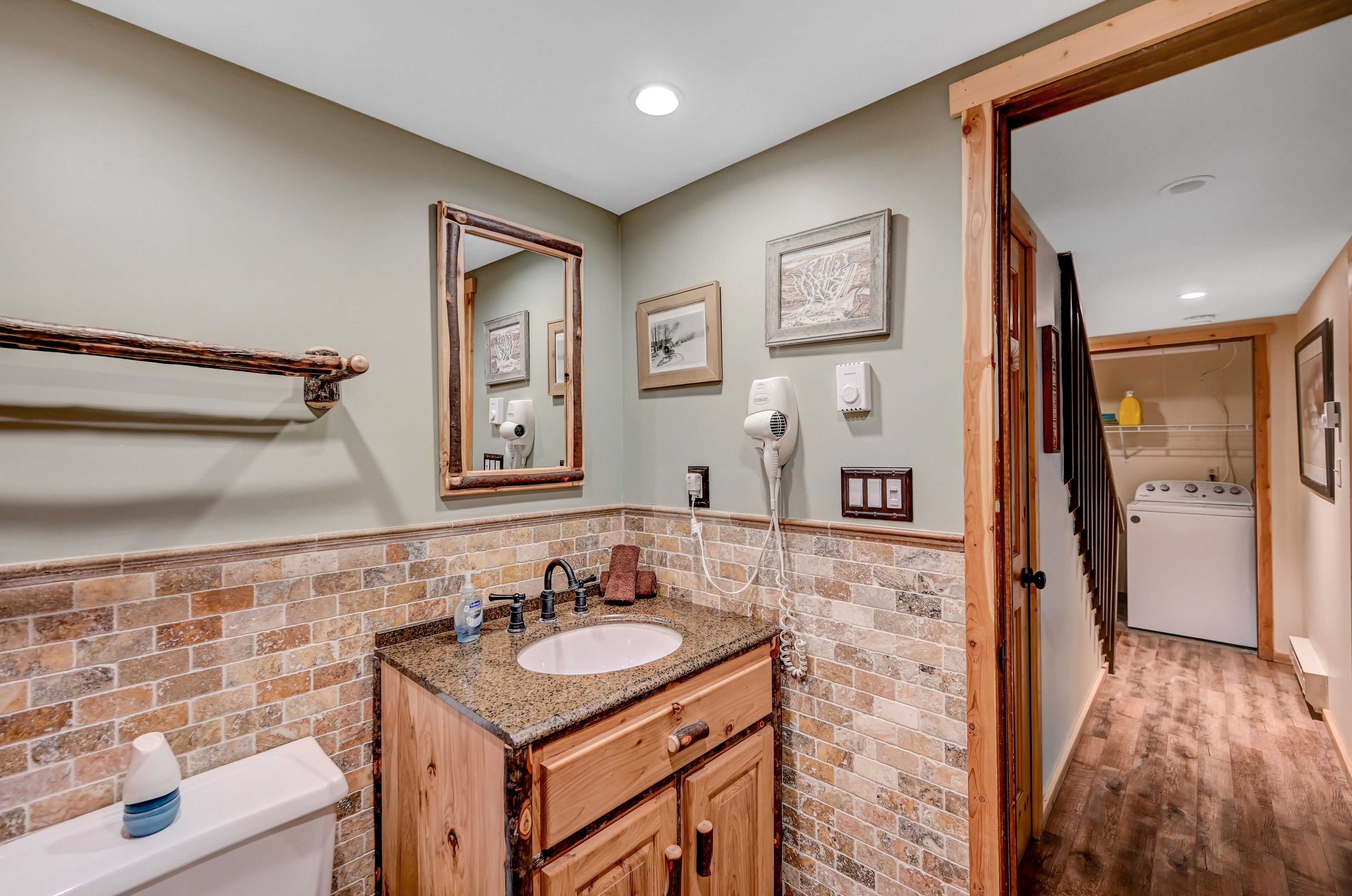 A bathroom with a sink, mirror, and towel rack. There is a wooden cabinet and a brick wall.
