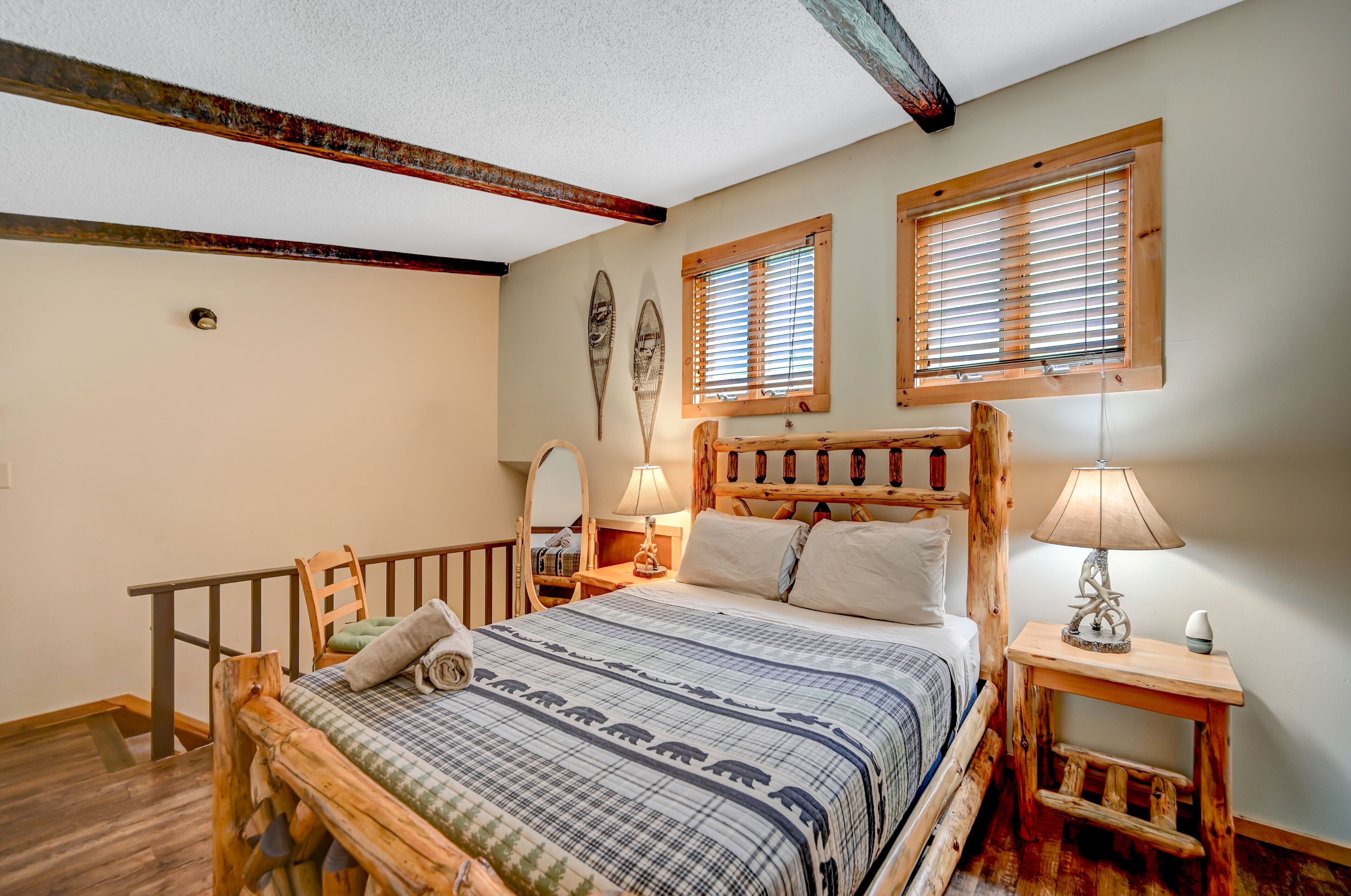 A cozy bedroom with a wooden bed, two bedside tables with lamps, a wooden headboard, and a window with blinds.