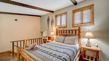 A cozy bedroom with a wooden bed, two bedside tables with lamps, a wooden headboard, and a window with blinds.