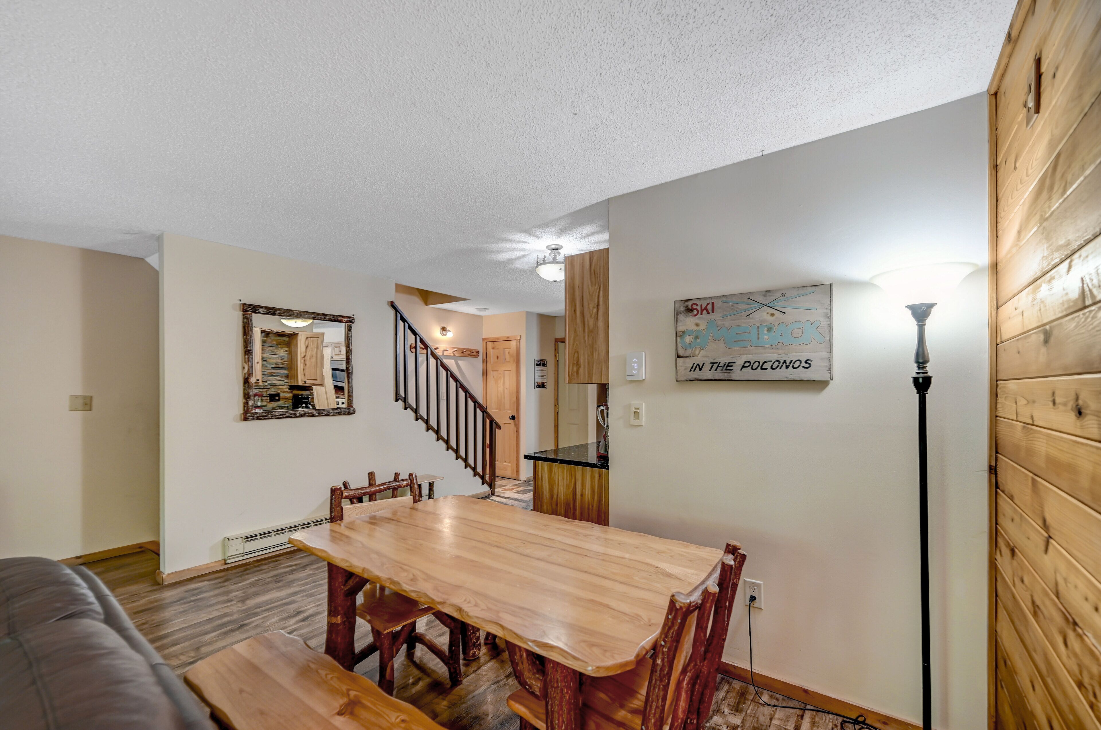 A dining area with a wooden table and chairs, a staircase leading to another room, and a wall-mounted sign.