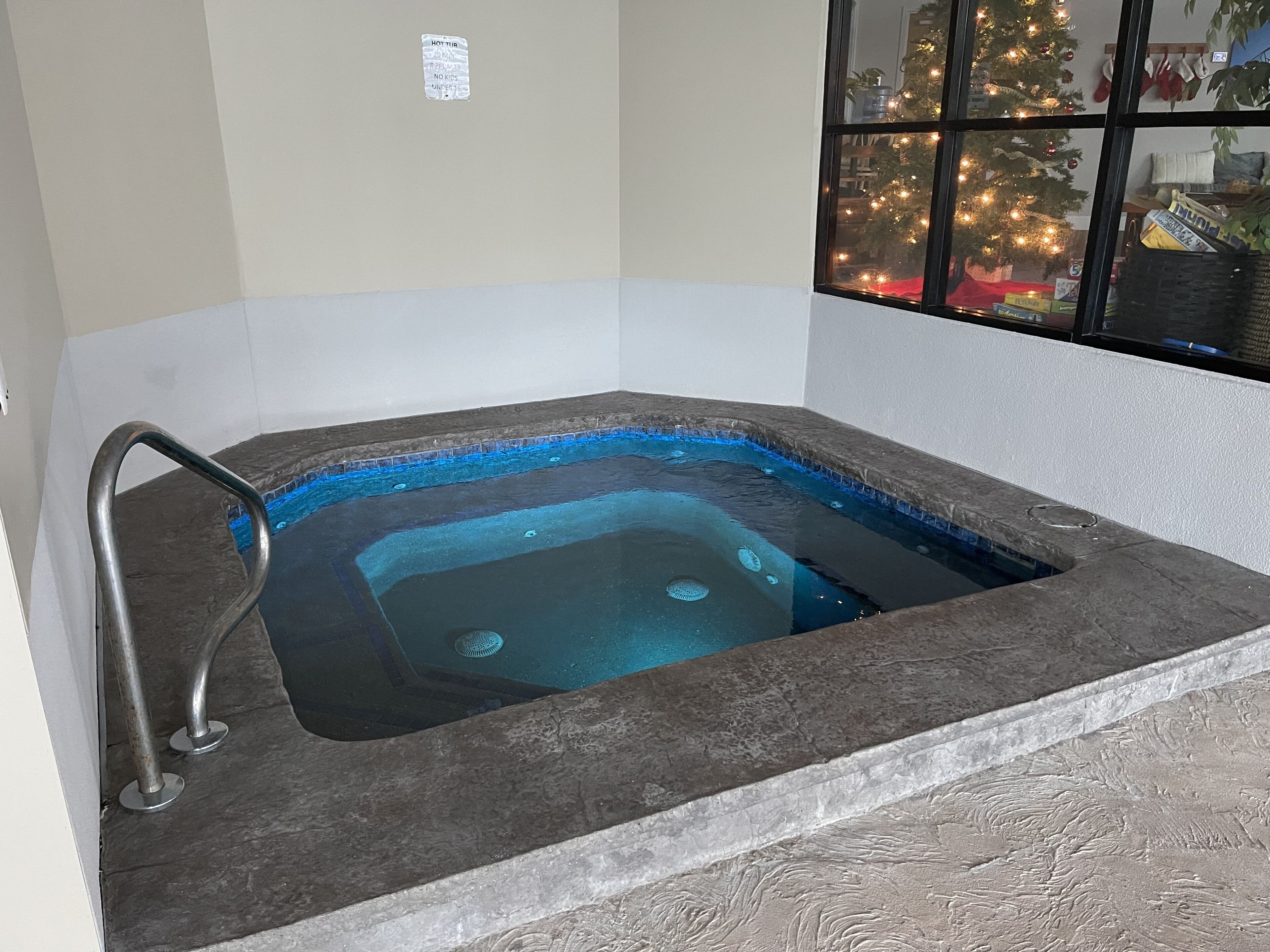 Jacuzzi amb un emmarcament de pedra, un grifer metàl·lic i vista a un arbre de Nadal decorat a través d'una finestra.