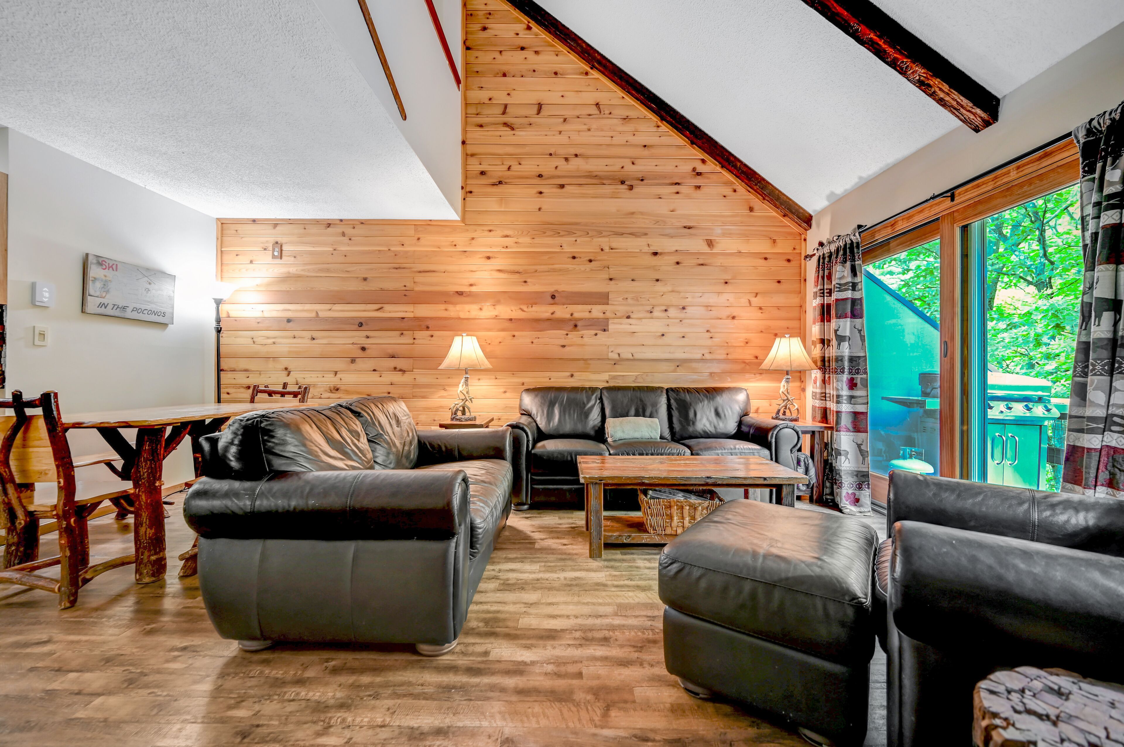 Una sala de estar acogedora con paredes de madera, un comedor con mesa de madera, y vistas a zonas verdes.